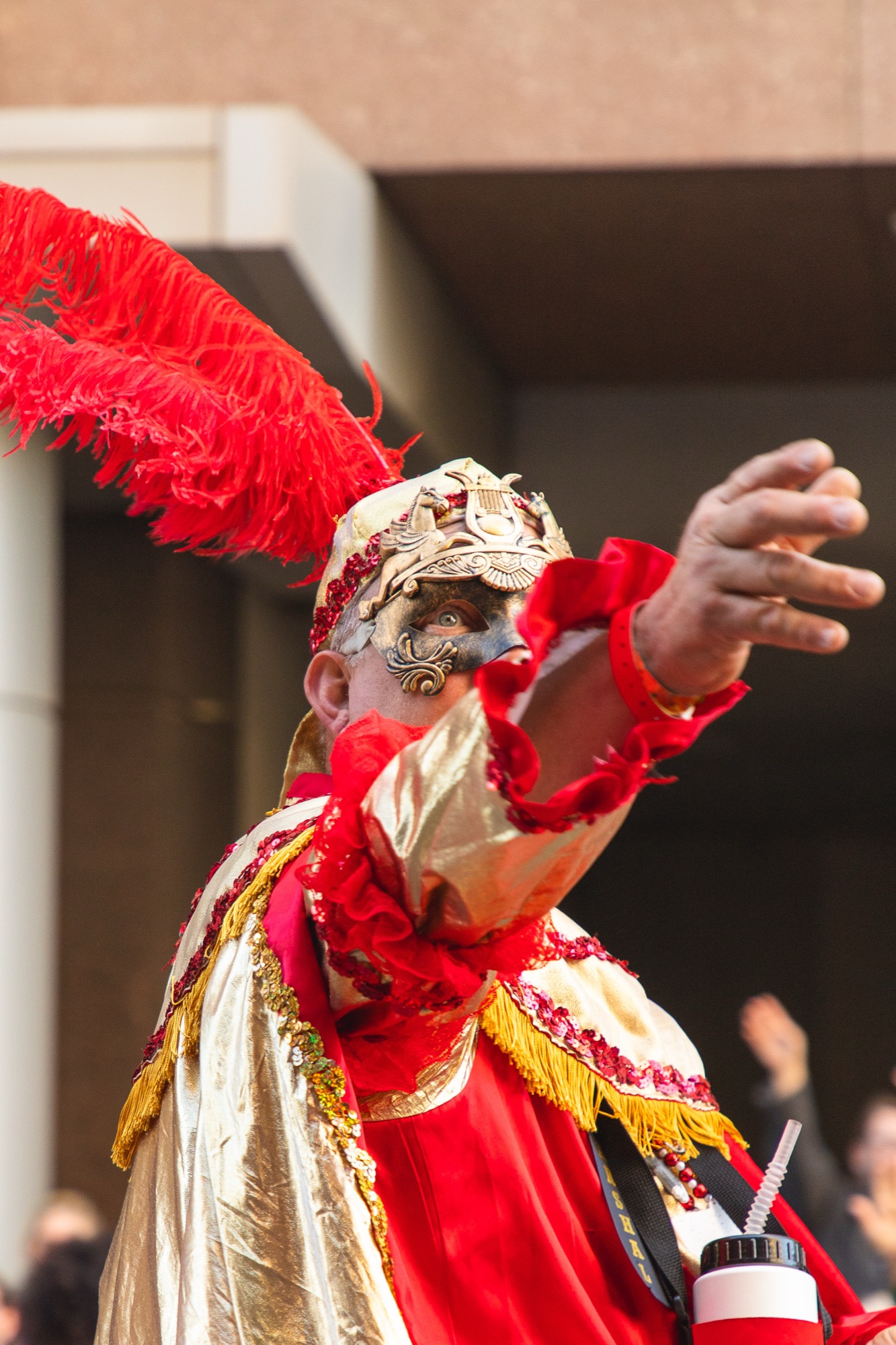 A masked parade marshal in red feathers waves to the crowd