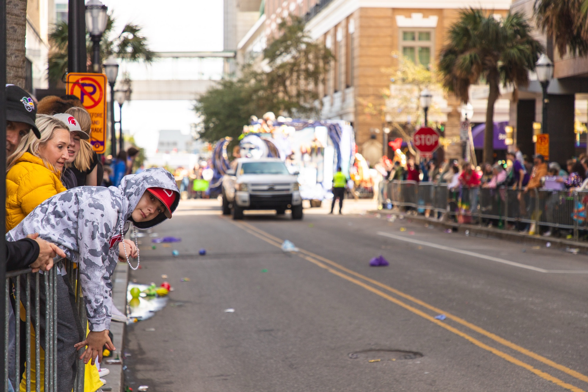 A kid leans over the barricade to watch the floats come up the street