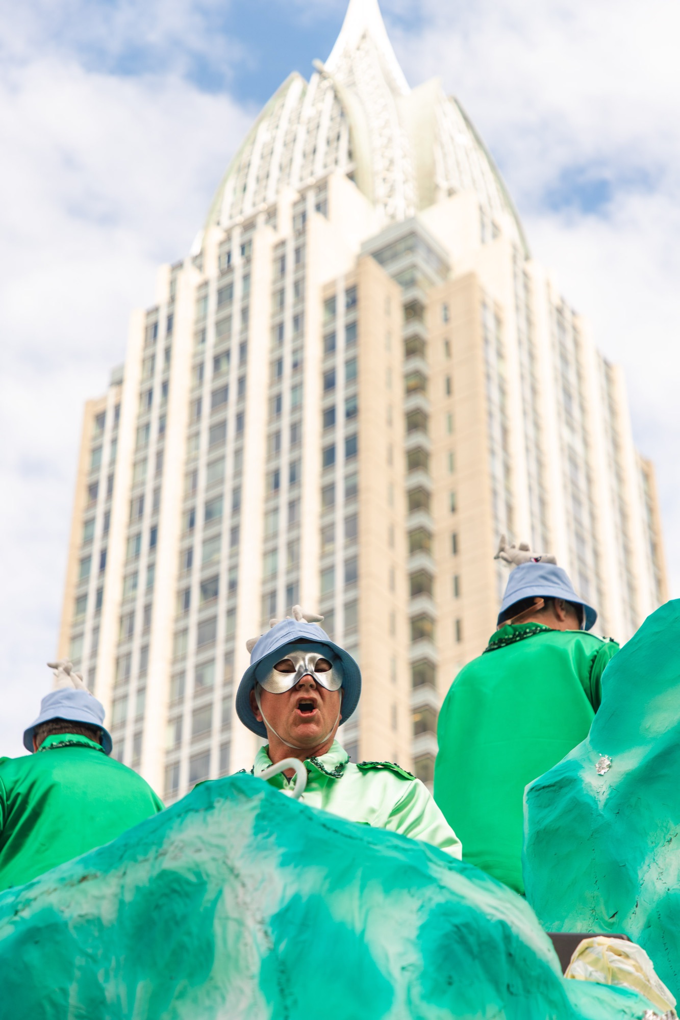 A masked krewe member in green, the RSA tower rising behind him