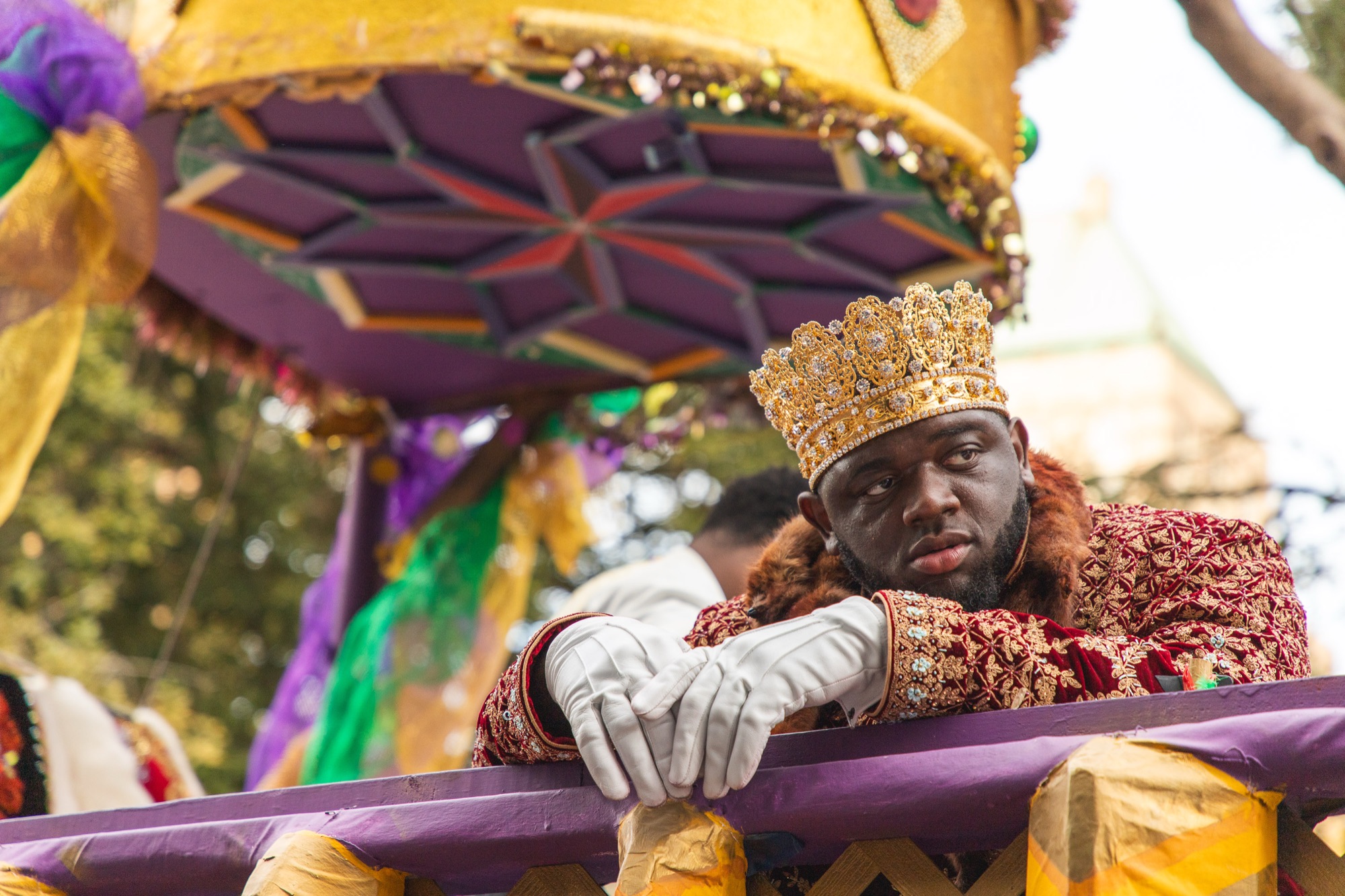 A Mardi Gras king in a gold crown leans on the rail of his float, deep in thought