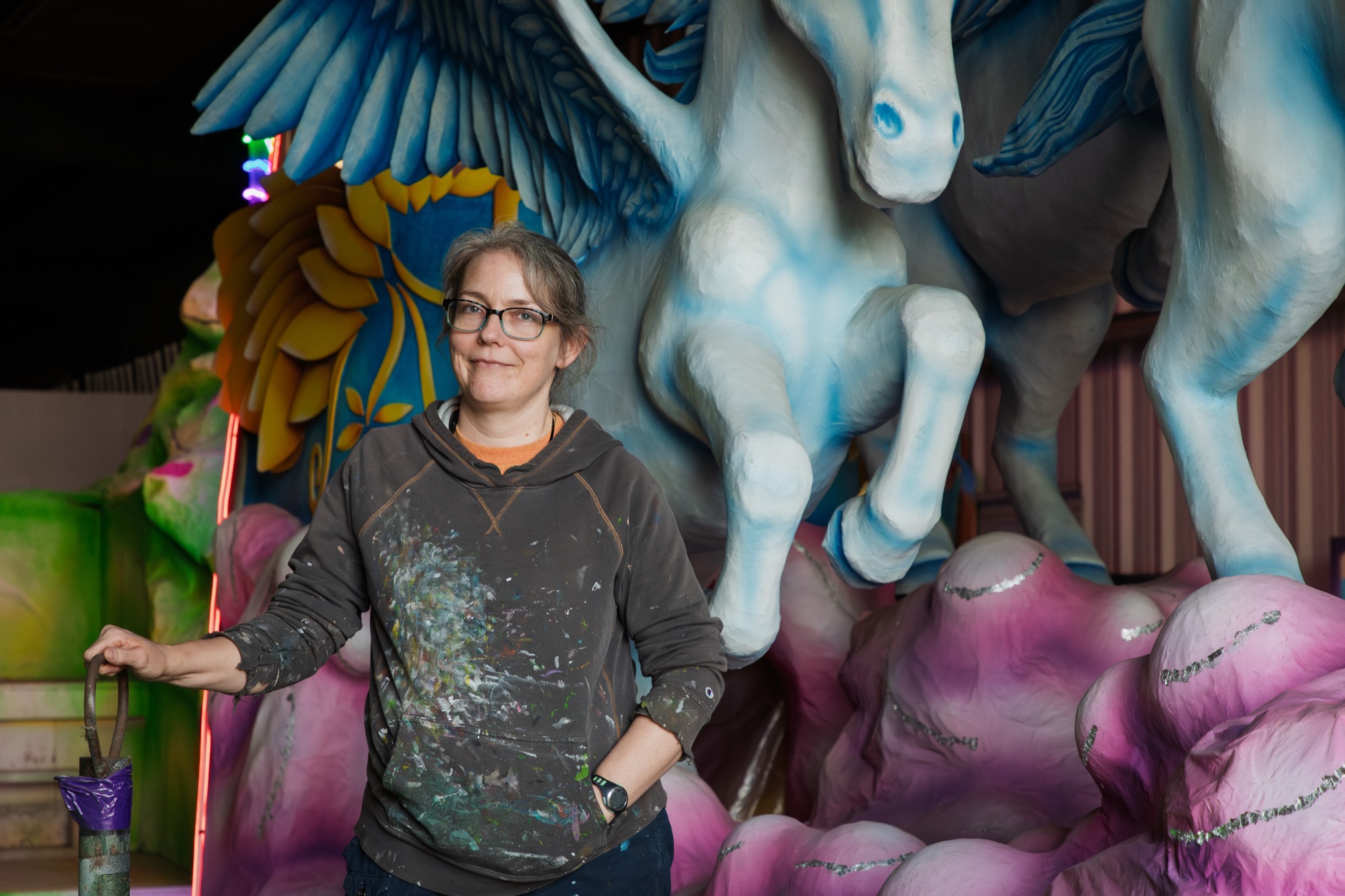 A float artist in a paint-splattered hoodie stands beneath a papier-mâché pegasus